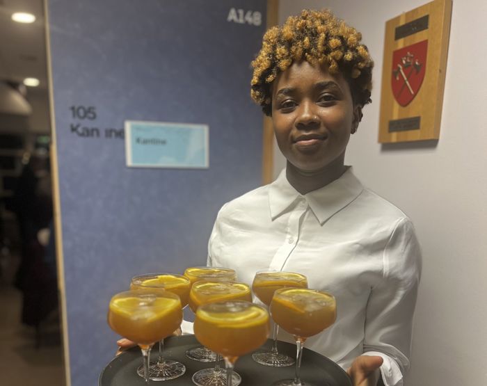 Elev i kvit skjorte med serveringsfat med glass med gul drikke oppi.