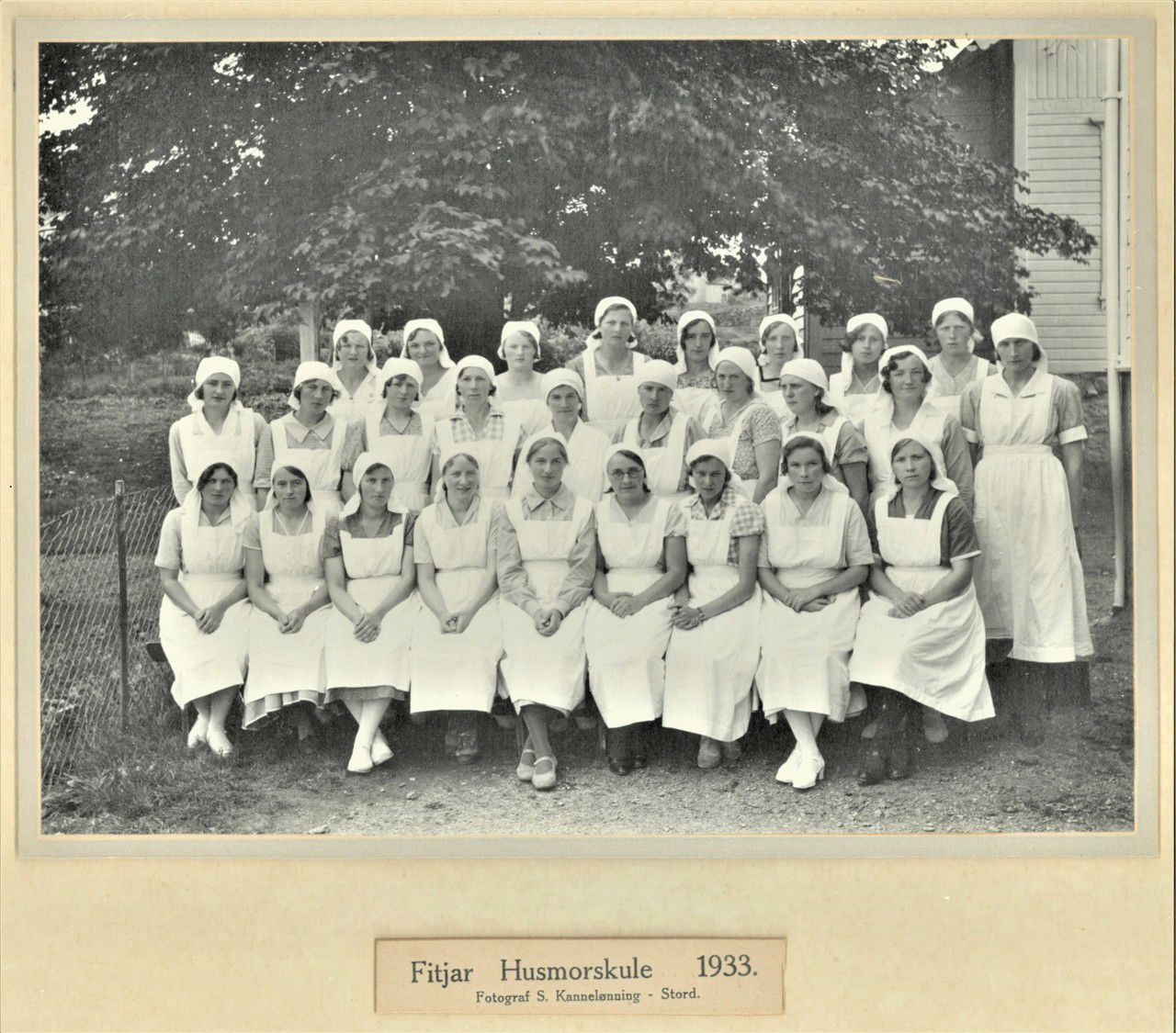 Eit klassebilete i svart kvitt frå 1933. Dei står oppstilt utanfor skulen og alle har kvite forklede og kvite skaut