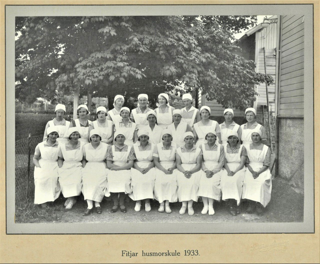 Eit klassebilete i svart kvitt frå 1933. Dei står oppstilt utanfor skulen og alle har kvite forklede og kvite skaut