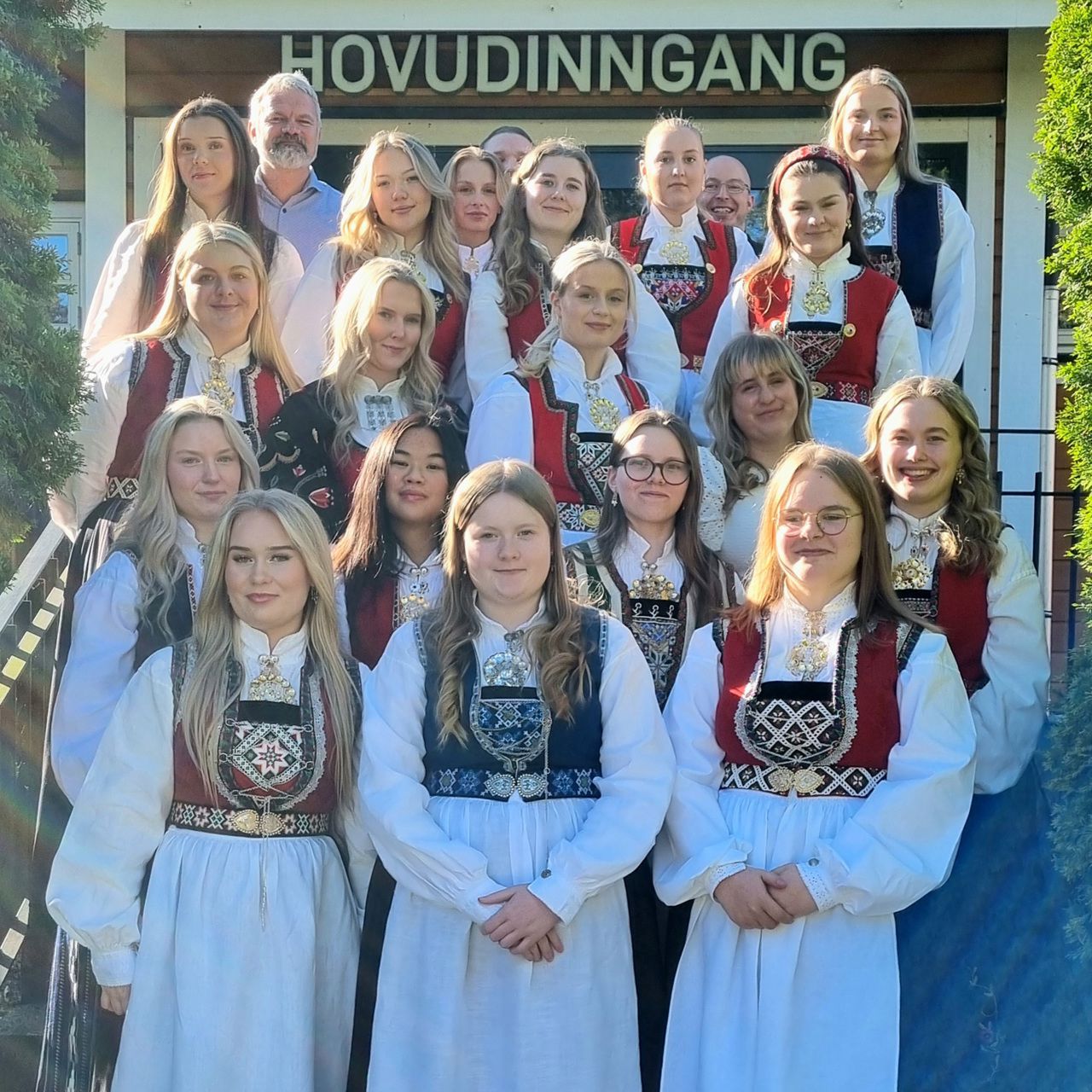Eit gruppefoto av skuleelevar i bunad. I bakgrunnen står lærarane. 