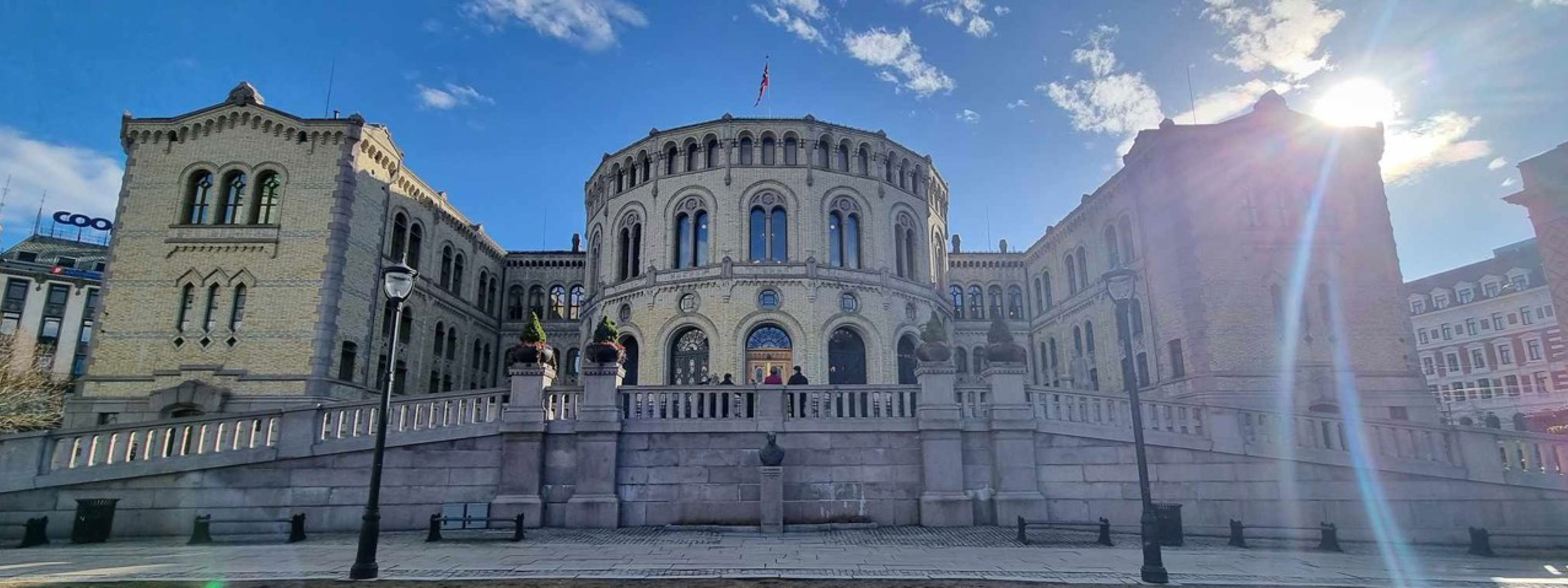 Det Norske Storting, sett utanfrå med blå himmel og sol bak