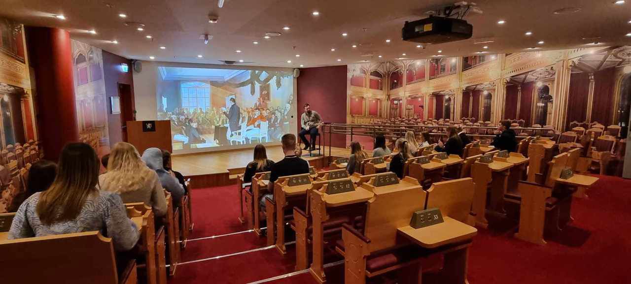 Masse elevar med ryggen til i eit klasserom som ser ut som ein stortingssal