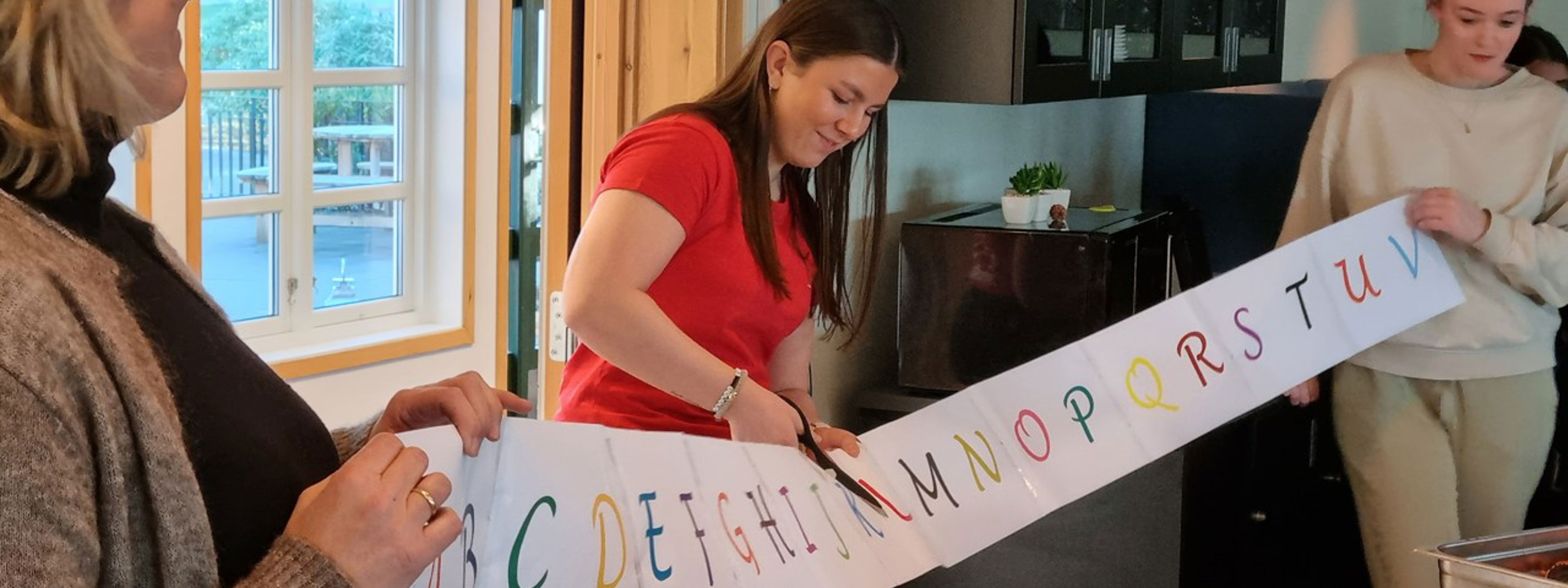 Elevrådsleiaren klipper over ei papirremse med alfabetet på