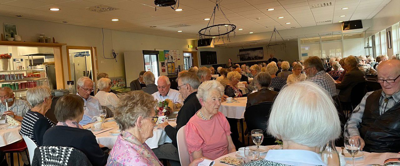 Mange eldre som sit i ei kantine ved dekka bord med kvit duk