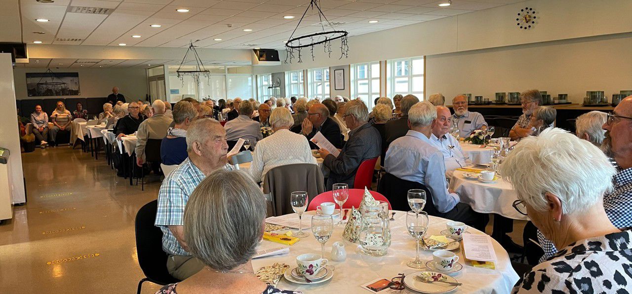 Mange eldre som sit i ei kantine ved dekka bord med kvit duk