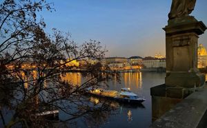Ei elv i Praha i skumringen, på elva er det ein båt, i framgrunnen er det ein statue
