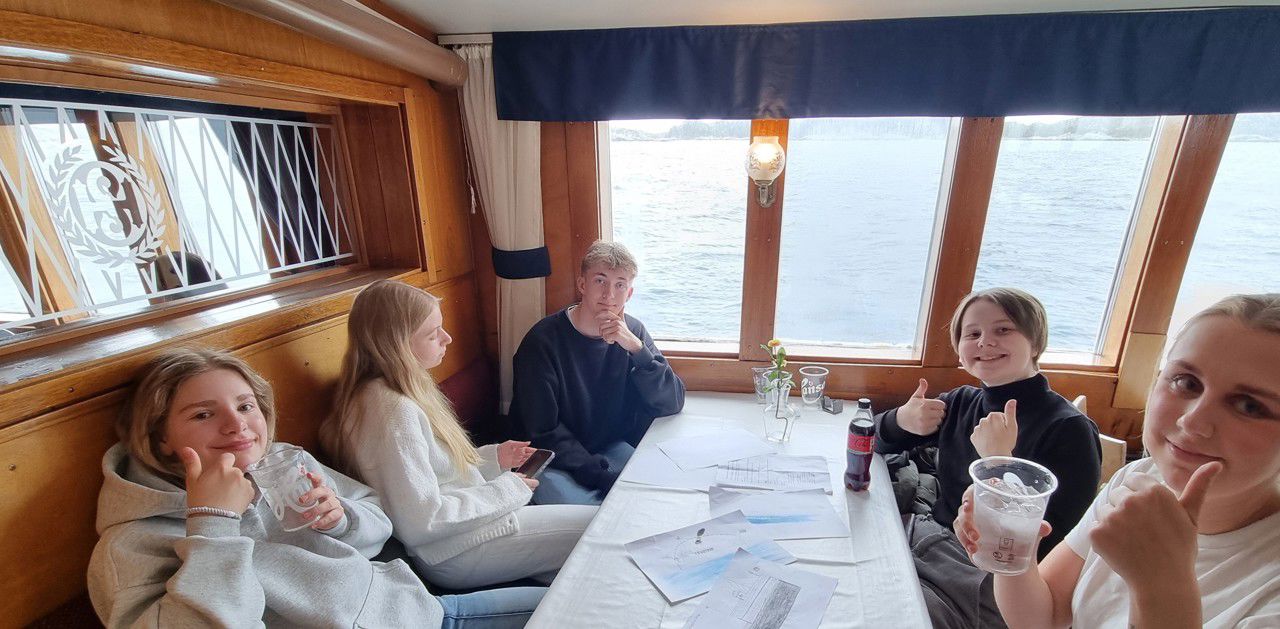 Fem elevar som sit ved eit bord, tre av dei viser tommel opp. 