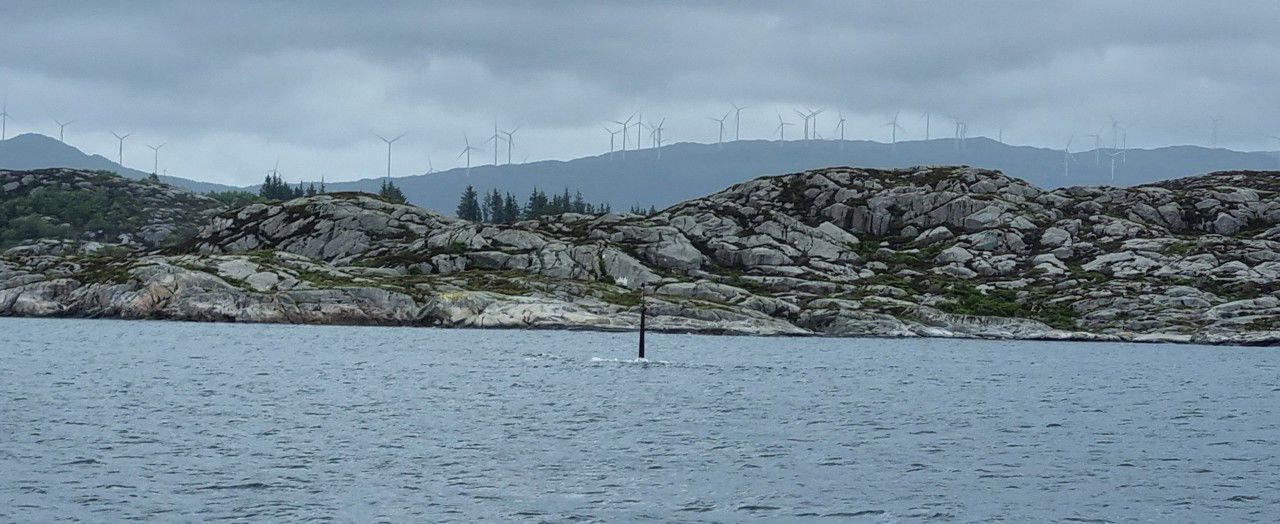 Me ser ei øy i Fitjar, og i bakgrunnen ser me Fitjarfjellet med vindmøllene