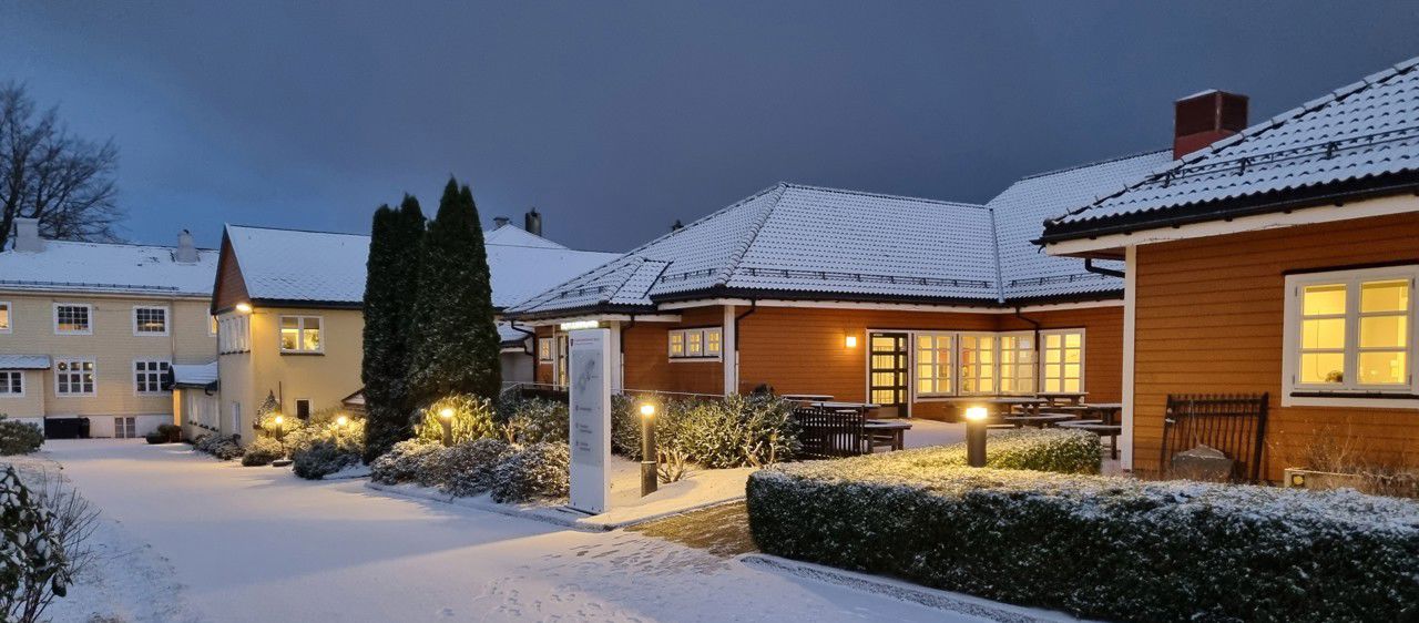 Eit bilete av skulen sett utanifrå. Det er snø og halvmørkt. Det er lys i skulebygget.