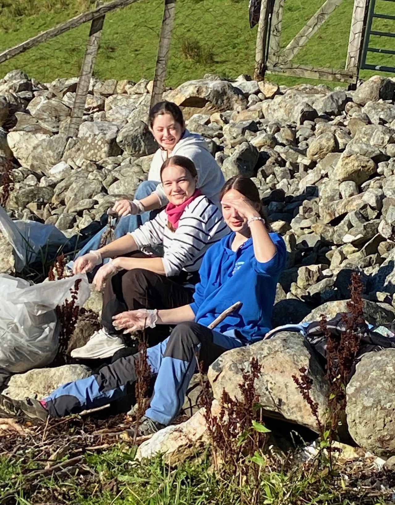 Tre elevar som sit i steinane og tek ein pause under strandryddinga