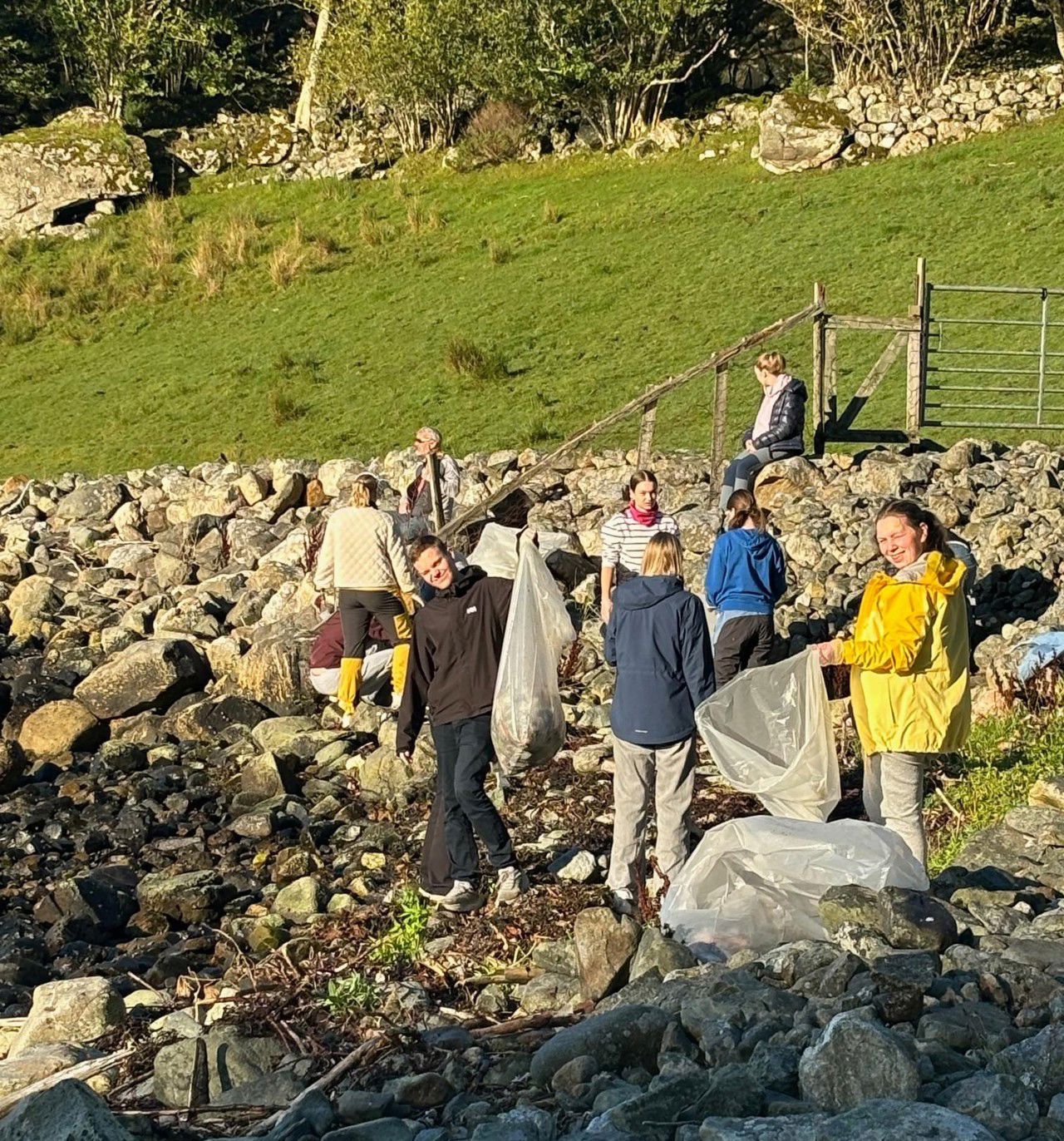 Elevar som går i ein stenfylt strand og plukker søppel i søppelsekkar