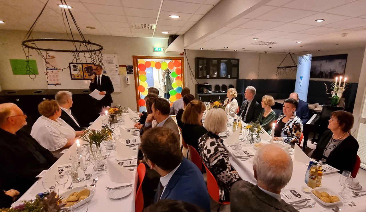 Mange folk ved eit pynta langbord, ein som talar i bakgrunnen