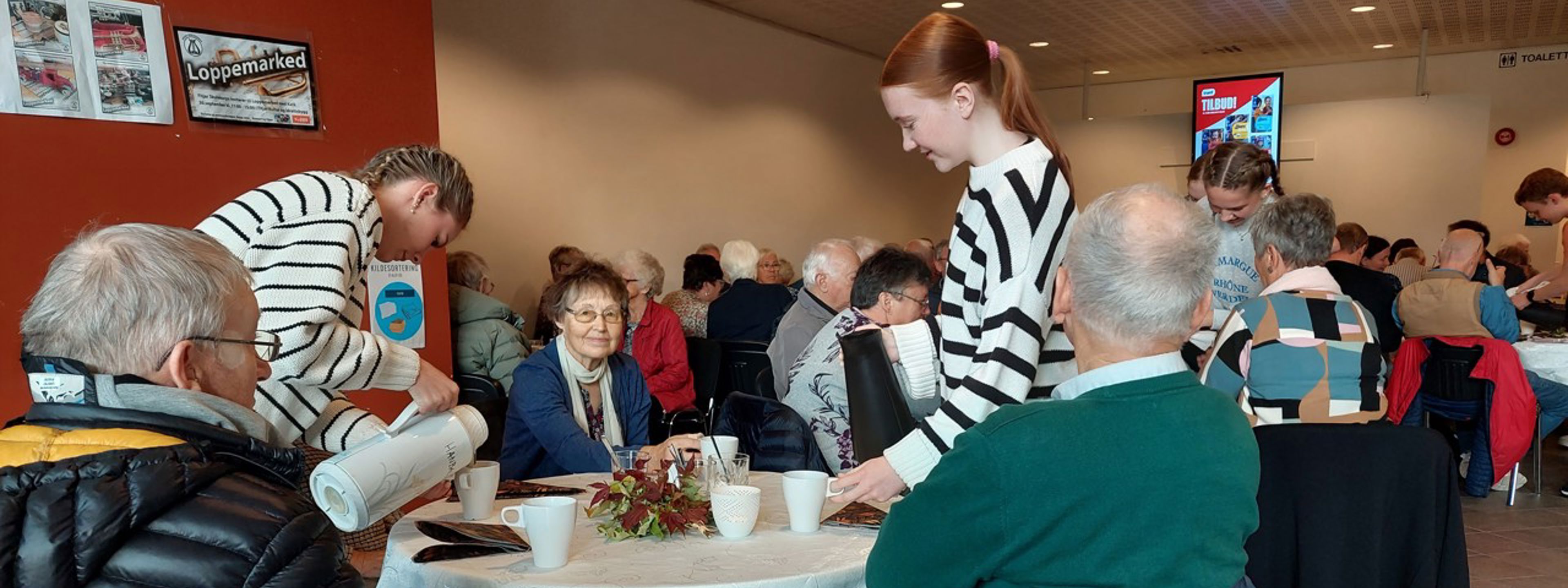Elev som serverer seniorar som sit ved eit bord