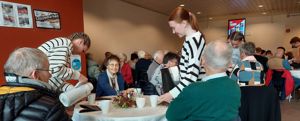 Elev som serverer seniorar som sit ved eit bord