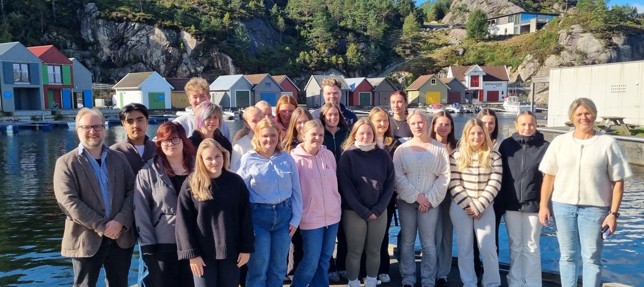 Ei gruppe elevar og to lærarar som står framfor vatn og nokre hytter. Det er elevrådet som er samla