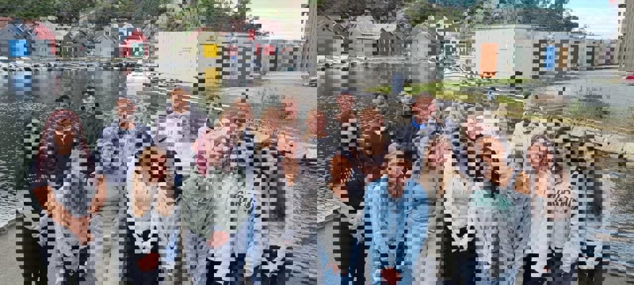 EI gruppe elevar som står framfor vatn og nokre hytter. Det er elevrådet som er samla